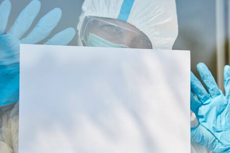 Disease control workers in protective clothing on door holding blank sign with copy space due to coronavirus pandemicの写真素材