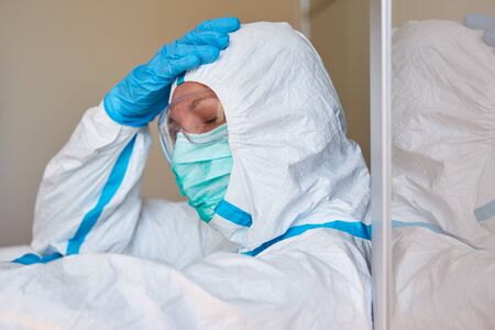 Doctor in protective clothing takes break due to burnout and exhaustion in coronavirus pandemicの写真素材