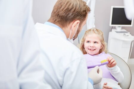 Pediatric dentist tells a girl with a giant toothbrush to brush her teeth as a precautionary measureの写真素材