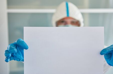 Disease control worker in protective clothing holds an empty notice board with copy space because of Covid-19 pandemicの写真素材