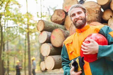 Young forest worker in protective clothing in front of a long wood cart at the wood harvestの写真素材