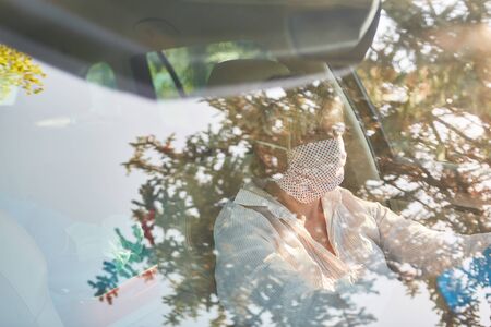 Looking through windshield at elderly woman with face mask due to coronavirus pandemic at the wheel of her carの写真素材