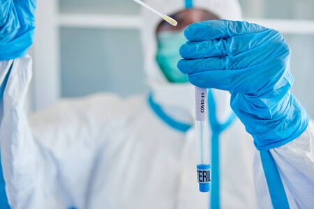 Medic in protective clothing packs throat swab from saliva sample for Covid-19 test