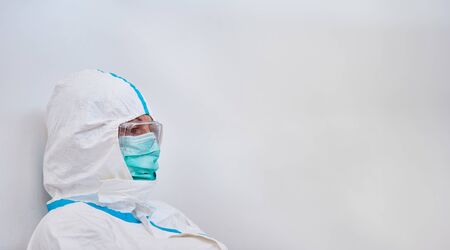 Doctor in protective clothing is thoughtful and exhausted during break during coronavirus pandemicの写真素材