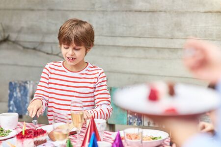 Merry boy is eating a piece of cake on the birthday party in the gardenの写真素材