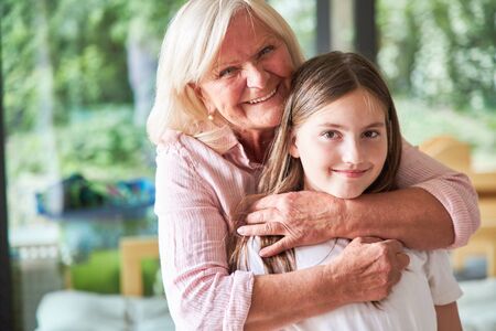 Granny lovingly hugs her granddaughter in the living room at homeの写真素材