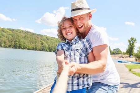 Boy in tug of war with his father at the lake in summer camp or summer vacationの写真素材