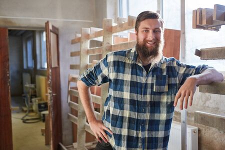 Smiling man with beard as a hipster carpenter in the carpentry workshop