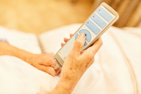 Hands of a senior citizen as a patient hold the remote control from the nursing bedの写真素材