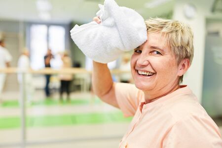 Happy senior woman with towel dries the sweat on her forehead after exercisingの写真素材