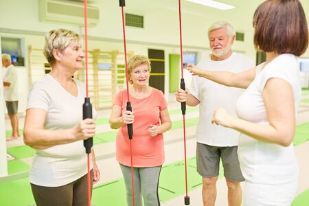 Seniors and fitness trainer with swinging bar for the back training in the fitness center