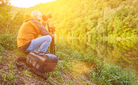 Old landscape photographer in nature at the river while photographingの写真素材