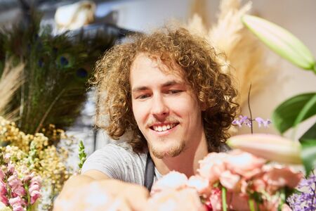 Young florist as trainee in flower shop between many cut flowersの写真素材