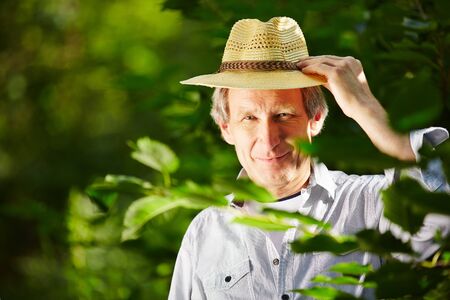 Senior with hat stands in summer smiling in natureの写真素材