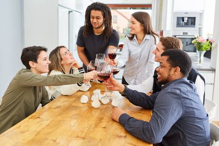 Happy friends toasting with a glass of red wine in the kitchen and celebratingの写真素材