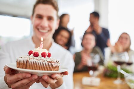 Young man gives cake with candle for birthday to friends in the kitchenの写真素材