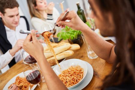 Friends eat spaghetti with tomato sauce together in the kitchen of a shared apartmentの写真素材