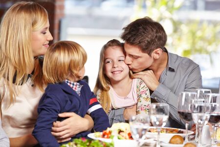 Father kisses daughter in the restaurant at lunch and mother and son watchの写真素材