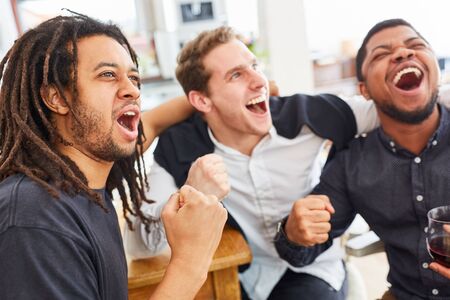 Friendly men cheer together while watching football at home