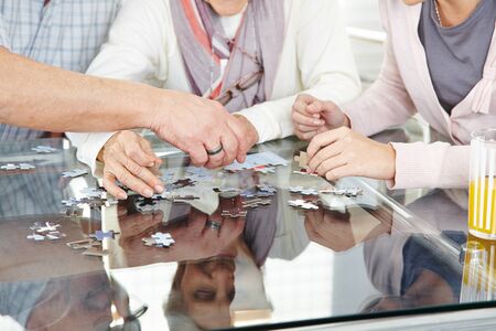 Hands of two seniors play puzzle with nurse in retirement home