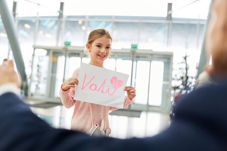 Girl greets her father at the airport on arrival with a sign reading "Vati" (German word for daddy)の写真素材