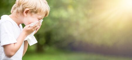Child with allergy in nature while sneezing into a handkerchiefの写真素材