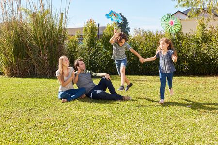 Two children play hilariously in the garden in summer with parents as spectators