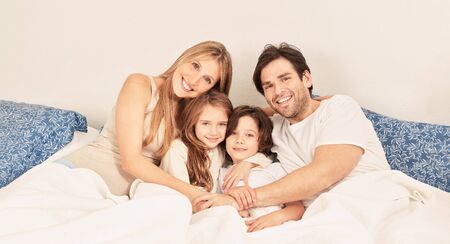 Happy family with two kids cuddling in bed as headers