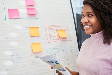 Creative African graphic designer on flipchart with graphics and sticky notes