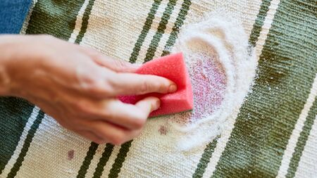 Hand with a sponge and salt while removing red wine stains on carpet