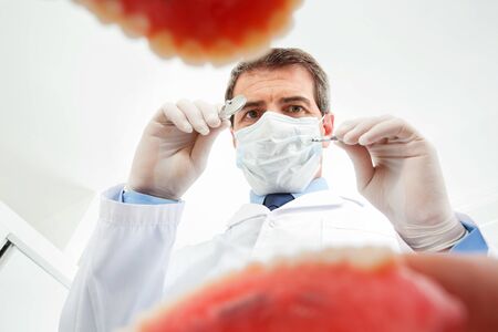 Dentist with face mask examines opened mouth