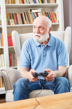 Senior man plays video game with console in living room as employmentの写真素材