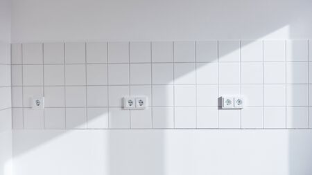 White wall with tiles and lots of sockets in empty kitchen at homeの写真素材