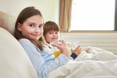 Sibling children drink orange juice for breakfast in bed in the bedroom