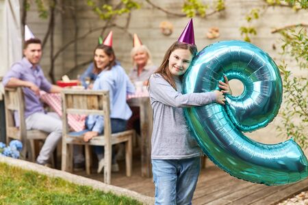 Girl celebrates birthday in the garden in summer with air balloon with the number nine