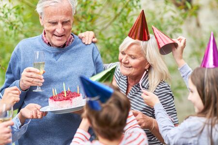 Children congratulate their grandfather with birthday cake in the summer gardenの写真素材