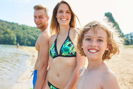 Happy parents with child on the beach in summer vacation by the sea or a bathing lakeの写真素材