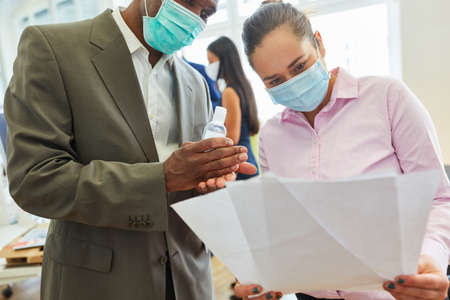 Two business people with mouth-nose protection because of Covid-19 read a document together