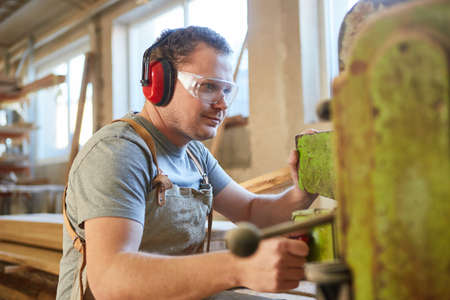 Carpenter apprentice with hearing protection on a woodworking machineの写真素材