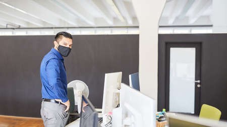 Young businessman in the office with face mask because of Covid-19 and coronavirus pandemicの写真素材