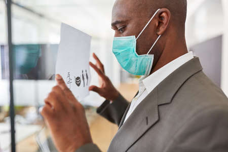 African businessman with mask because of Covid-10 fastens notice board with hygiene concept in...