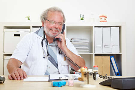 Friendly elderly doctor is talking on the phone in his practiceの写真素材