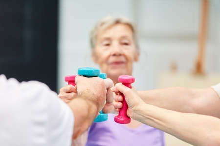 Senior woman with other seniors working together on dumbbell training in rehabの写真素材