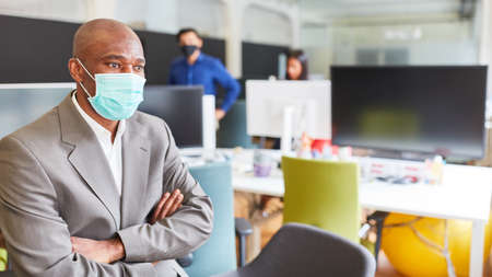 Thoughtful African business man or consultant with face mask because of Covid-19 in the office