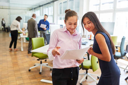 Two young business women discuss a document or project in the start-up office