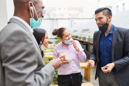 Business people having small talk and eating together in a break with face mask on chin