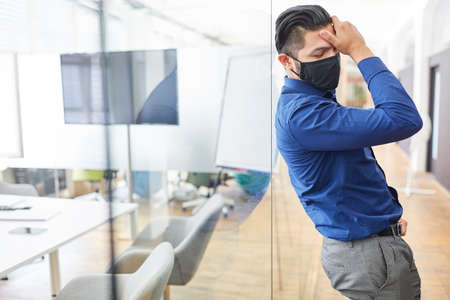 Business man with face mask because of Covid-19 after termination touches his forehead exhausted