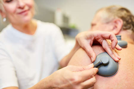 Female doctor makes pain therapy in senior patient and attaches vacuum electrodes to the body