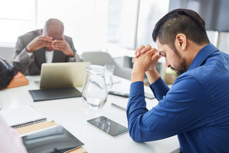 Desperate and sad business people sitting at conference table after bankruptcy or layoff