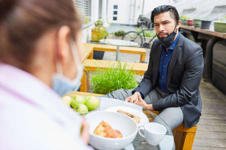 Business man with face mask on chin sits during lunch break in cafe with a colleagueの写真素材